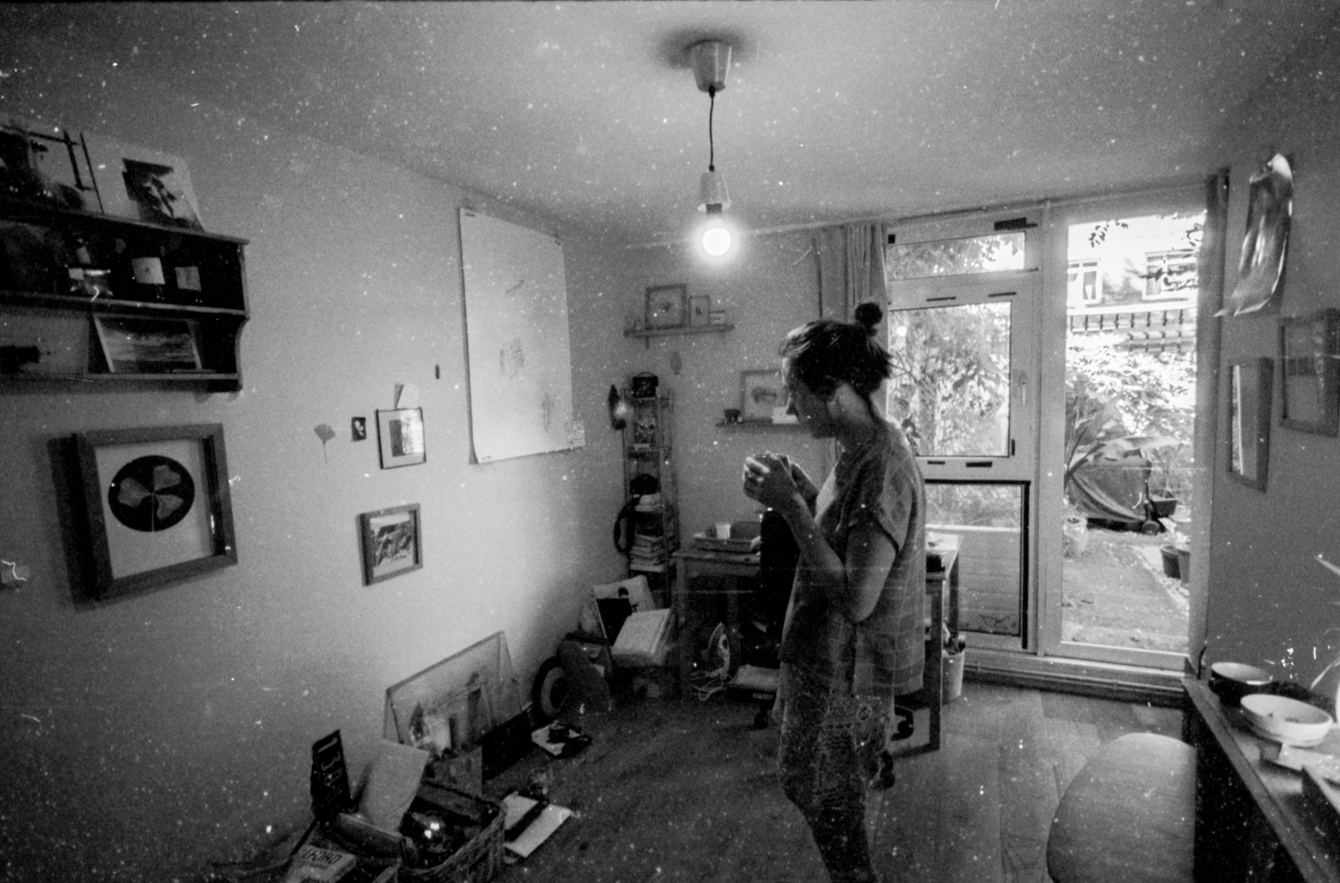 Zwart-wit foto van Alice Cazenave staand in een kamer, met een kopje in de hand, kijkend naar de muur.