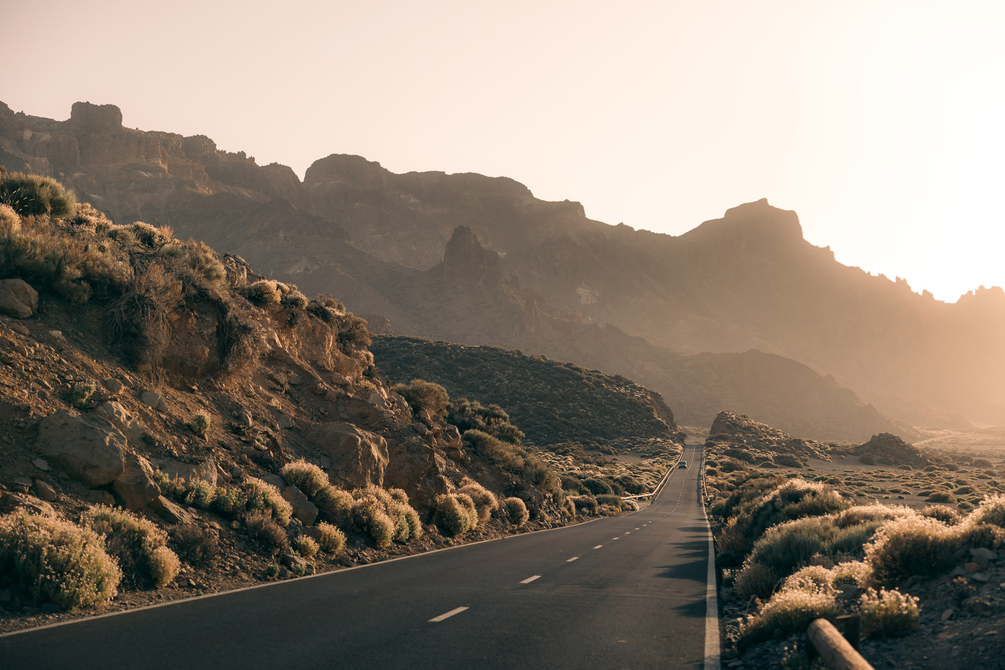 A road leads towards a mountain range with bright sun in the background, created with a Canon EOS R5 body and Canon RF 24-70mm f/2.8 L IS USM lens by travel photographer Harry Pope
