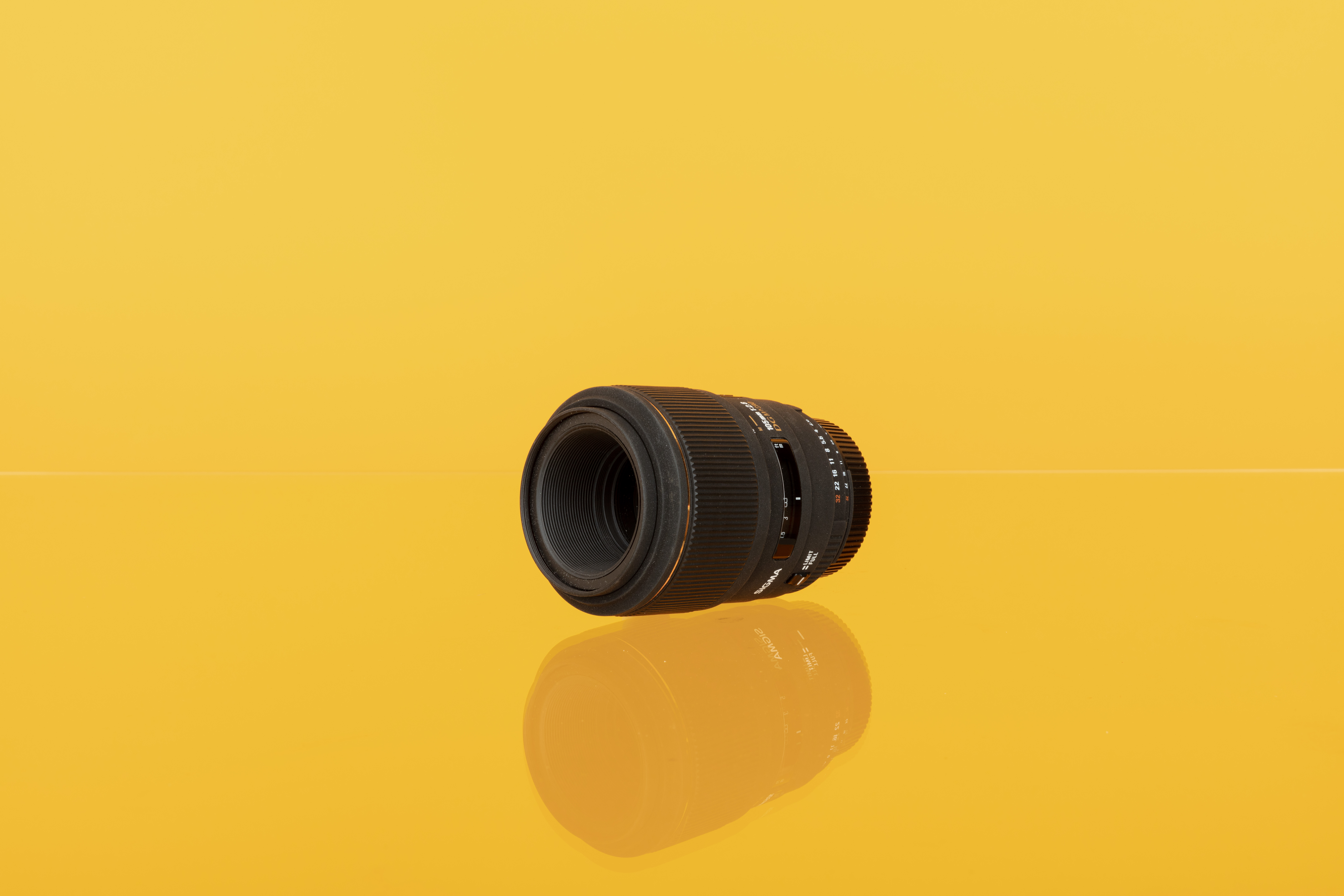 Image of a Sigma 105mm f/2.8 EX DG Macro OS HSM lens on a yellow background.