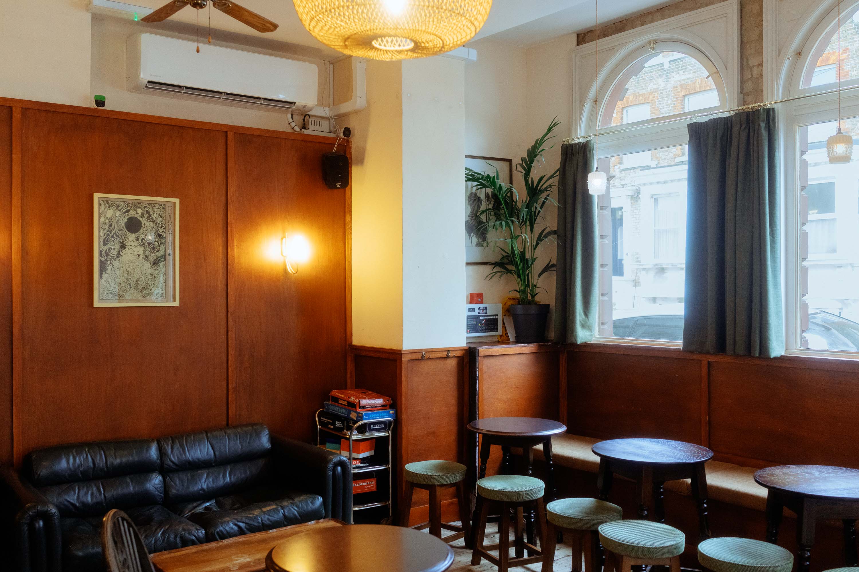 Ein gemütliches Pub-Interieur mit Holzvertäfelung, kleinen runden Tischen, Hockern an Rundbogenfenstern und warmer Umgebungsbeleuchtung, fotografiert bei weichem, natürlichem Tageslicht. Aufgenommen von Connor Redmond mit einer Sony RX1R III.