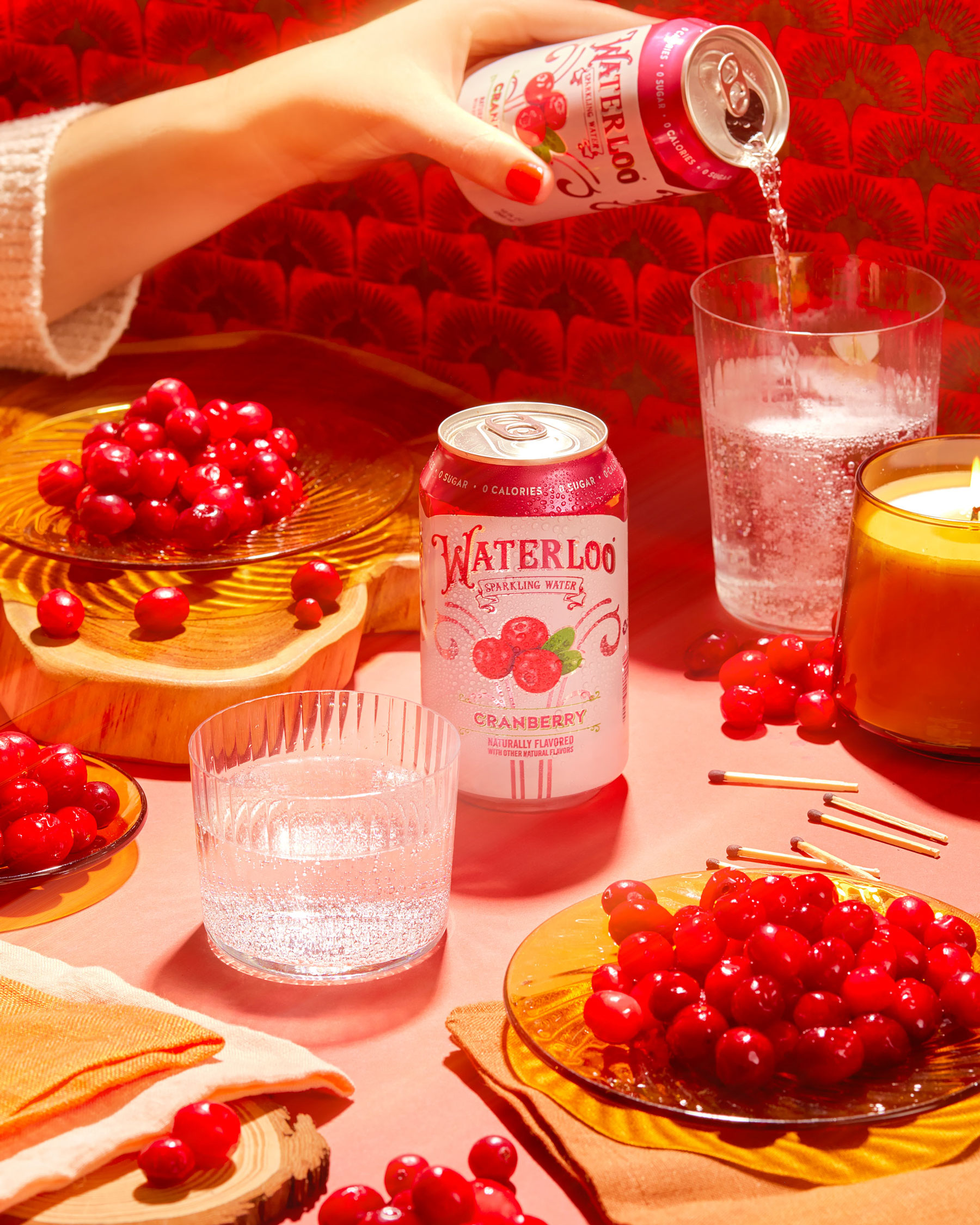 Hand pouring Waterloo drink into a cup on a table covered in cranberries.
