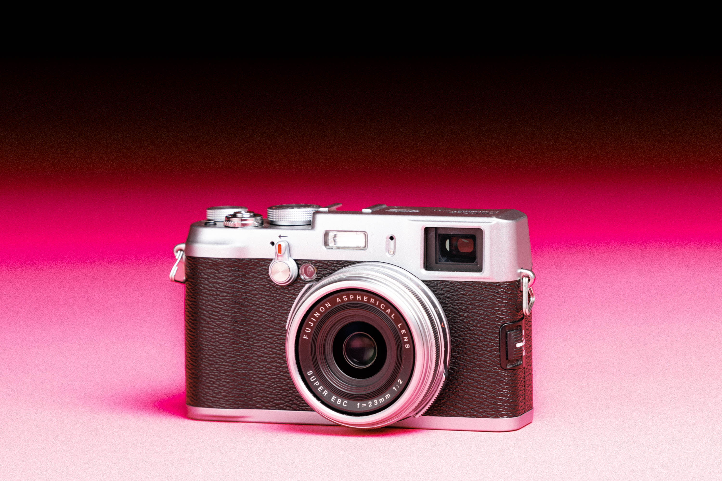  A used Fujifilm X100VI with an added film-like grain effect on a graduated pink background.