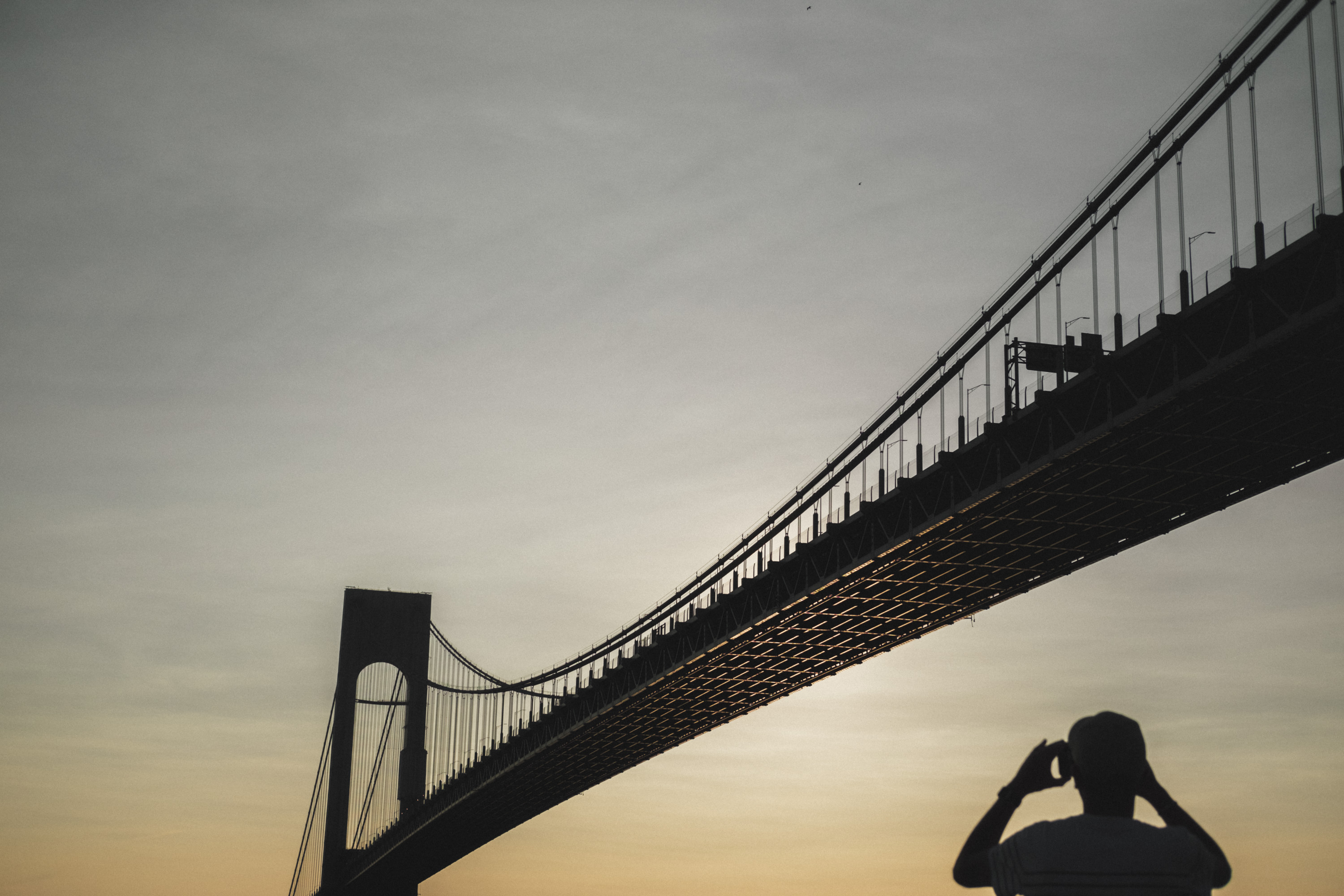 The Verrazzano-Narrows Bridge at sunset with a tourist silhouetted taking a picture. Shot on the X-Pro 3 by Ian Howorth.