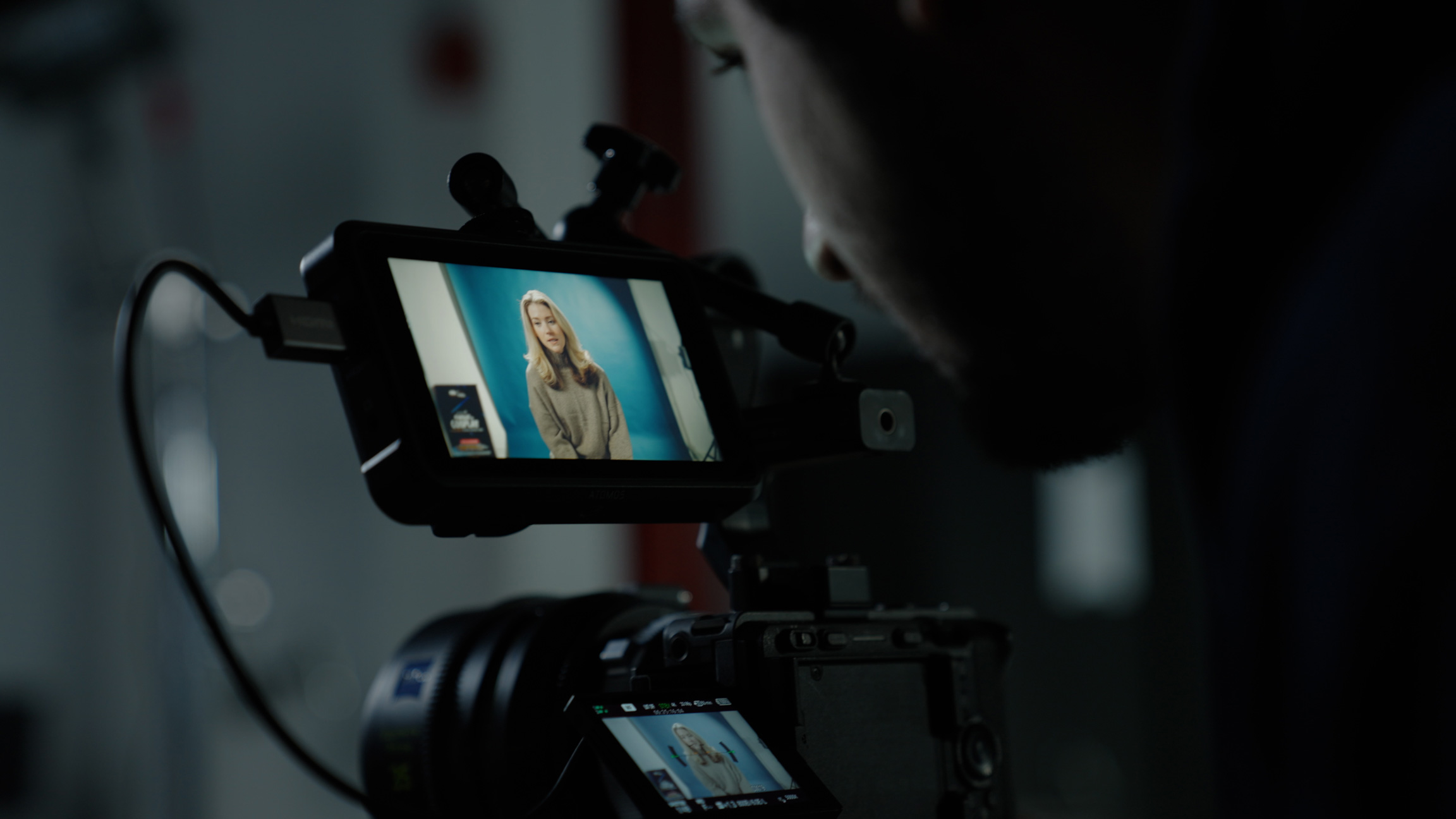 Moody photo of person looking closely at monitor on top of camera in a dark room
