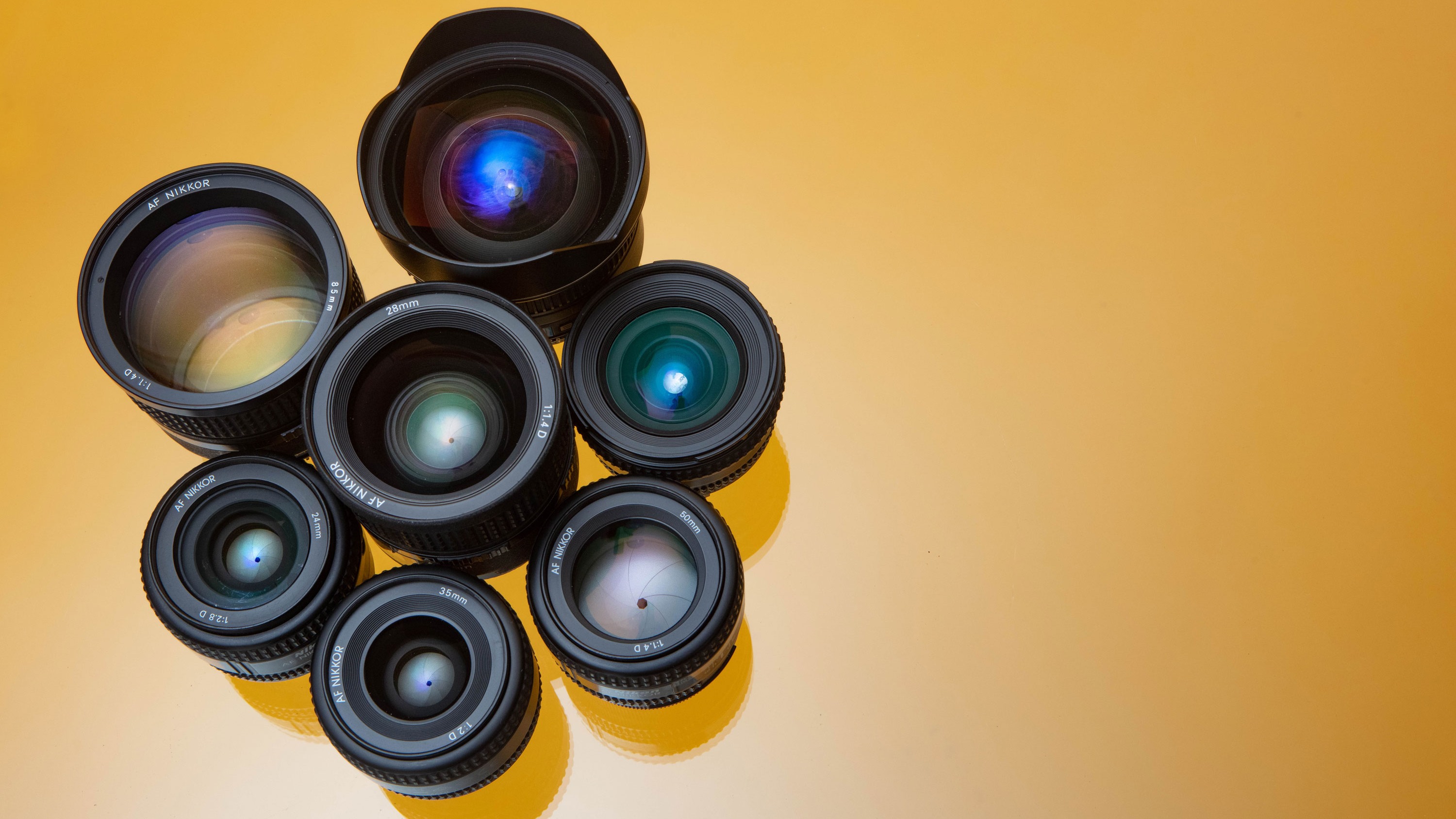 Un ensemble d'objectifs Nikon disposés en cercle sur un fond jaune.

