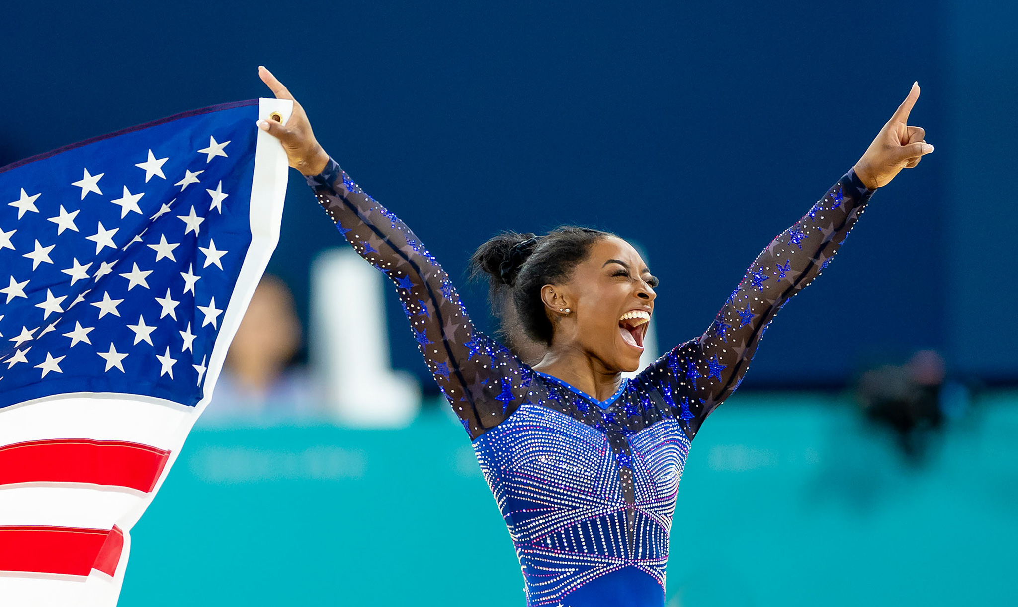 Simone Biles celebrates whilst holding the American flag in one hand. By Iris van den Broek.