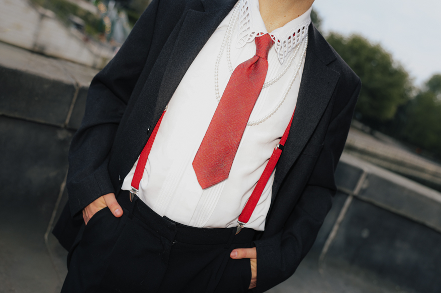 A close-up of a wedding suit showing a red tie, suspenders, and pearls styled with a black suit. Shot by Marina Polovinkina on the Canon EOS R6 Mark II.