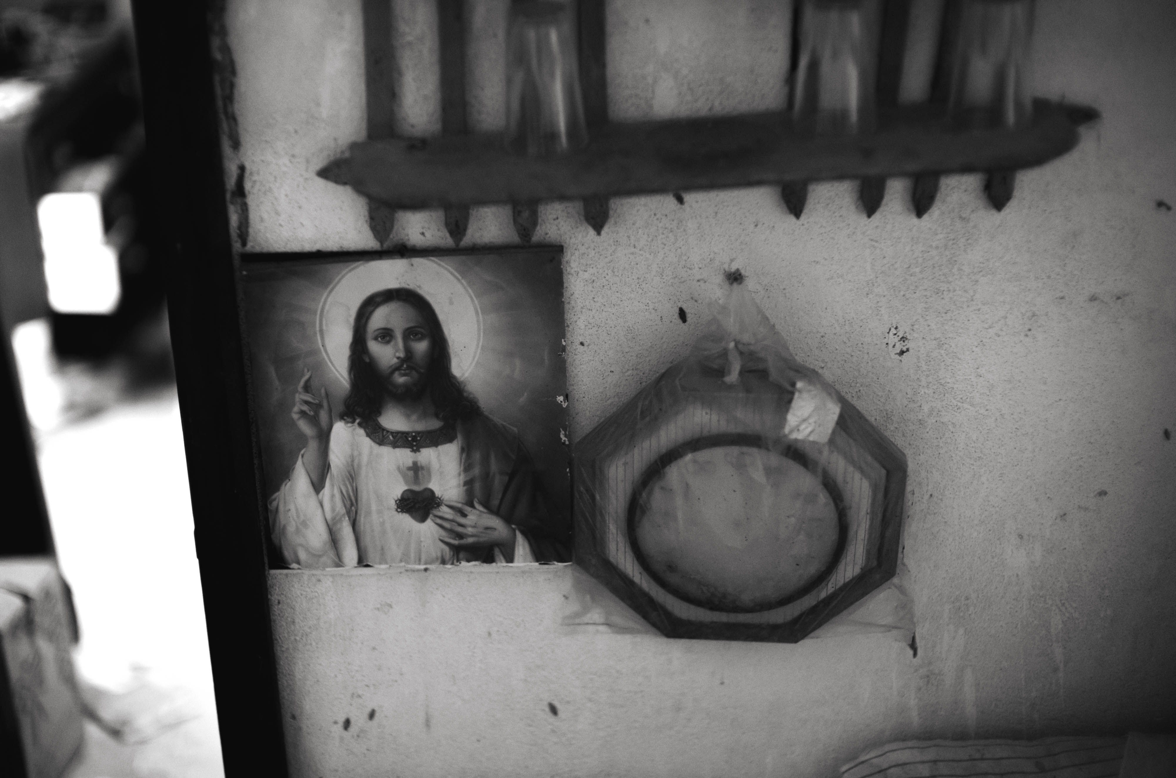 Une photo en noir et blanc d'une icône de Jésus sur un mur entouré d'une étagère et d'une décoration en bois, prise avec un Leica M10 Monochrom.