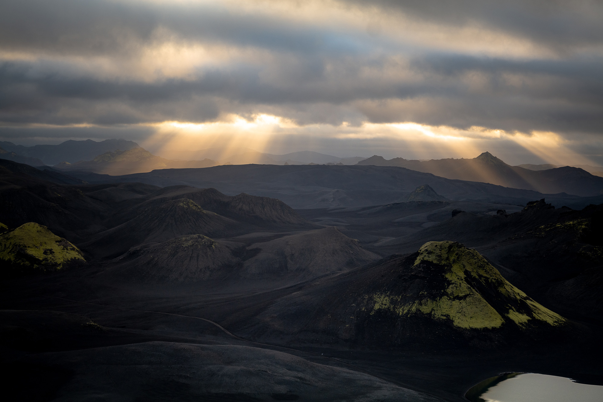 A landscape photo of rays of sun peeking through clouds over a mountain range in Iceland at sunset, shot by Paul Watson with a Panasonic S1R
