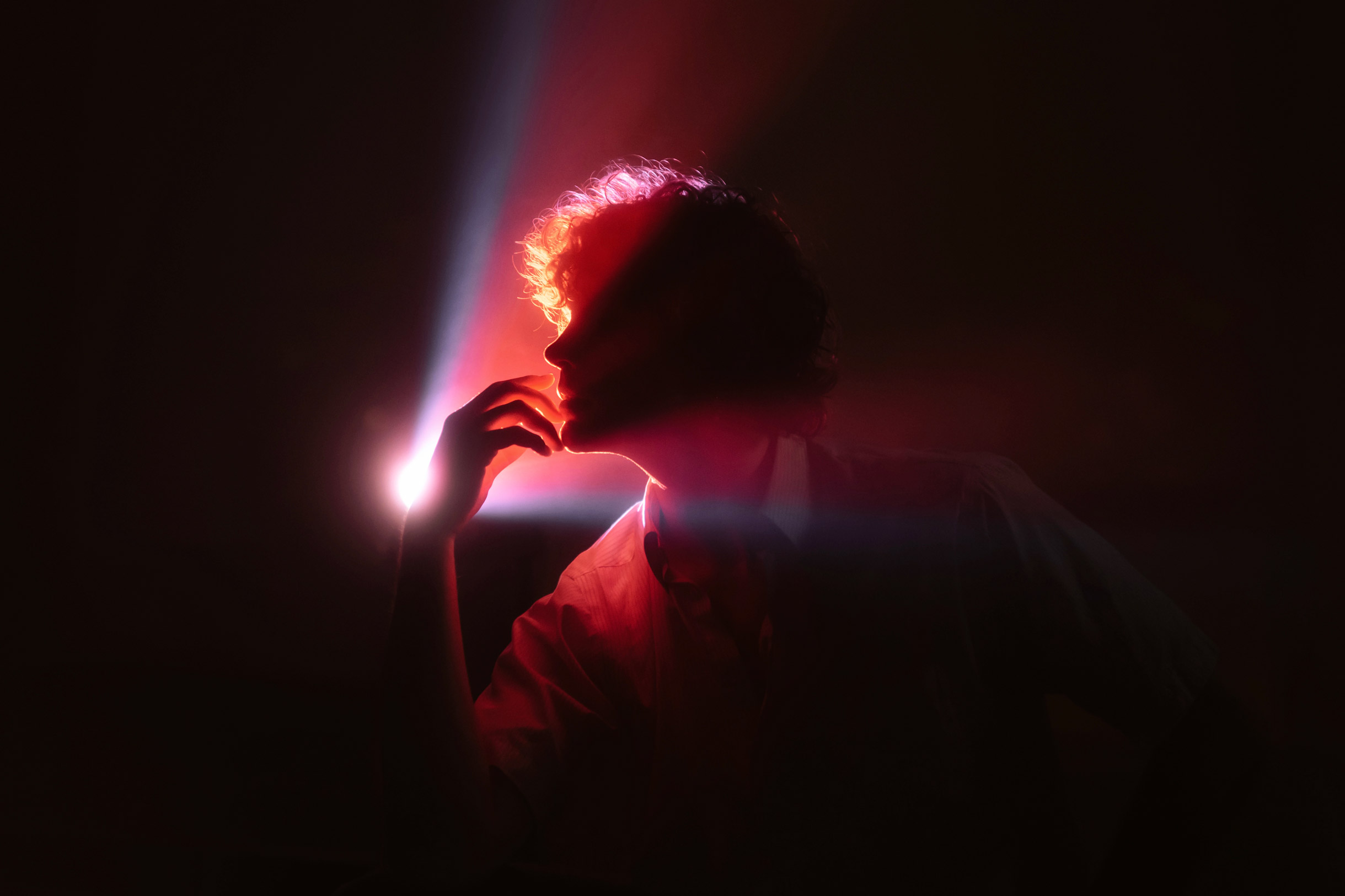 Silhouette of person with hand against face with blue and red light shining on head, photo by Brandon Woelfel