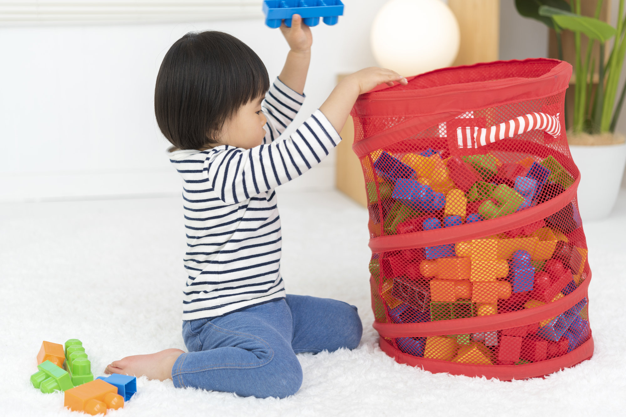 Bé châu Á dọn đồ chơi vào giỏ trong không gian gọn gàng