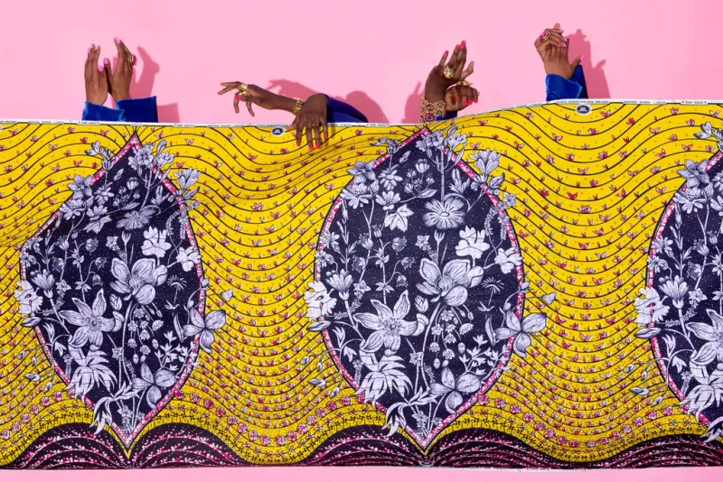 Women's hands appearing above a Vlisco fabric representing an abstract vagina with a bouquet of flowers