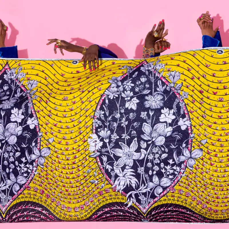 Des mains de femmes apparaissant au-dessus d'un tissu Vlisco représentant un vagin abstrait avec un bouquet de fleurs