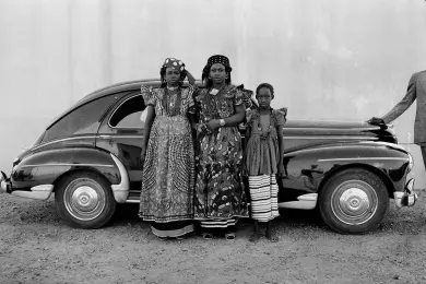 Une photographie prise par Seydou Keïta de 3 femmes africaines en imprimé africain Vlisco devant une ancienne voiture