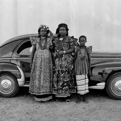 A photograph taken by Seydou Keïta of 3 african women in Vlisco african print in front of an old car