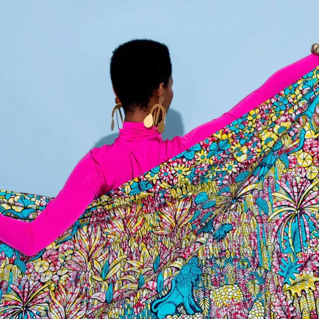 A women facing away holding a Vlisco fabric representing lions in a jungle