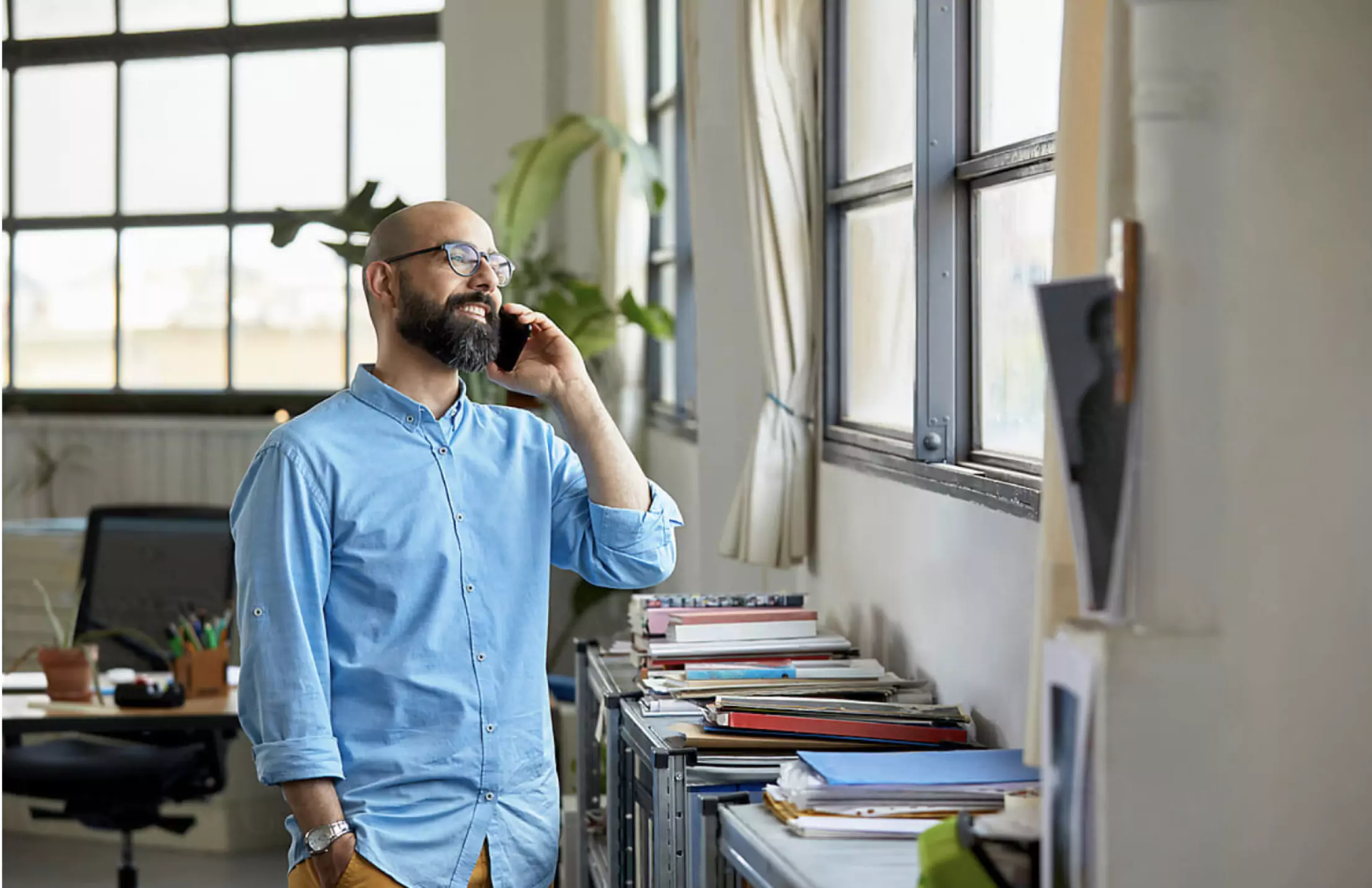 Man with glasses speaking on the phone while looking out an office window