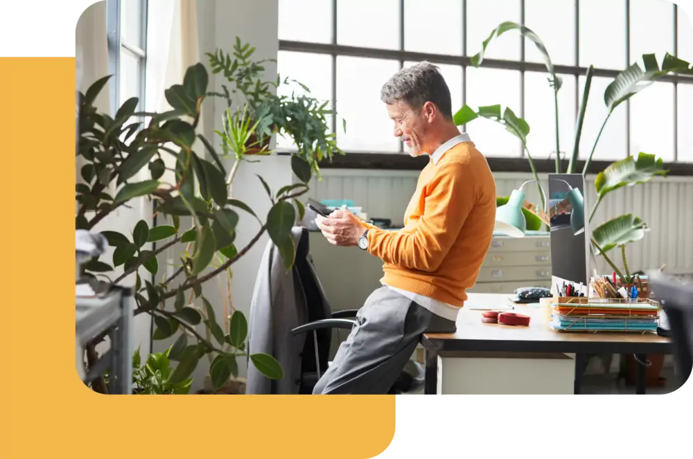 Photo of a man looking at his phone in a plant-filled office