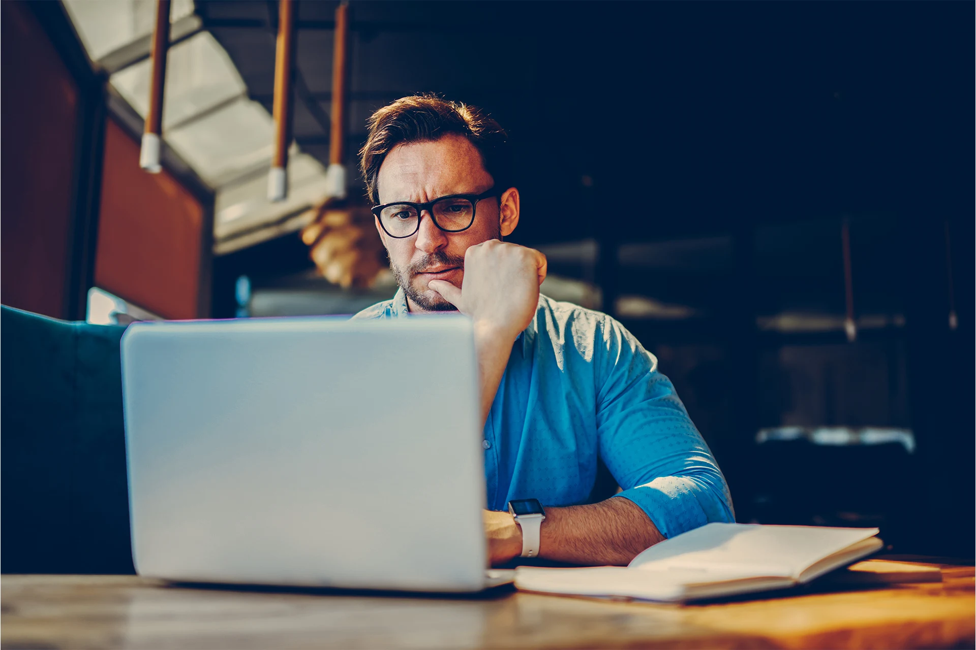 Professional working on a laptop with a notebook at a workspace
