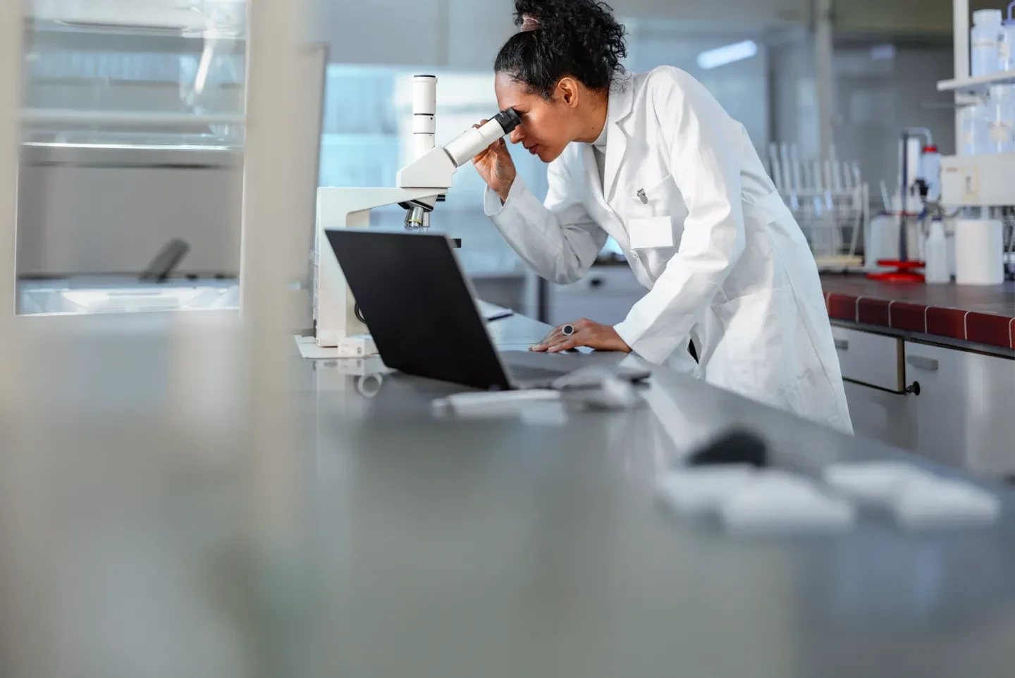 Scientist examining samples under a microscope in a laboratory setting.