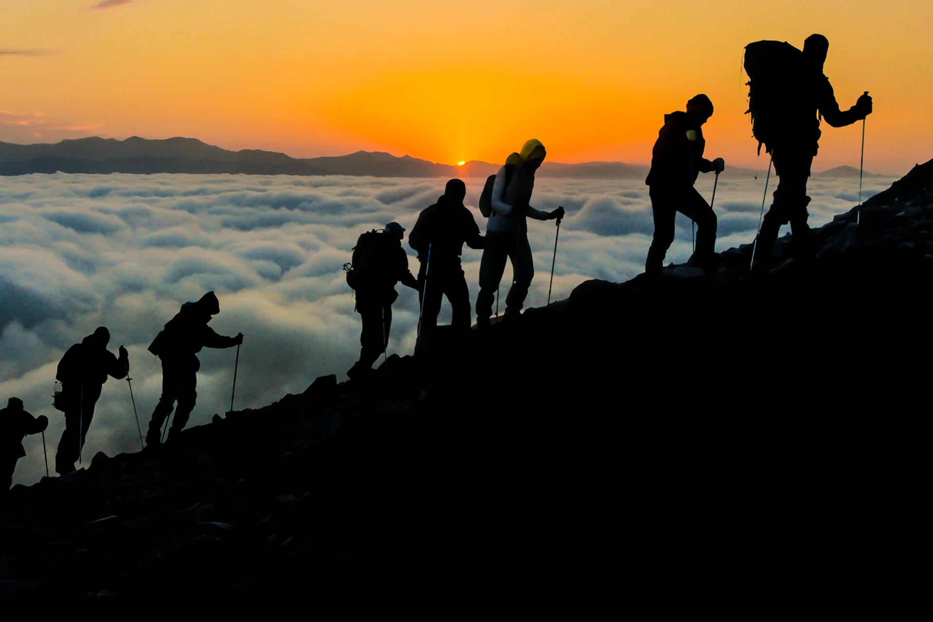 Hikers ascending a mountain above the clouds representing ambition and growth