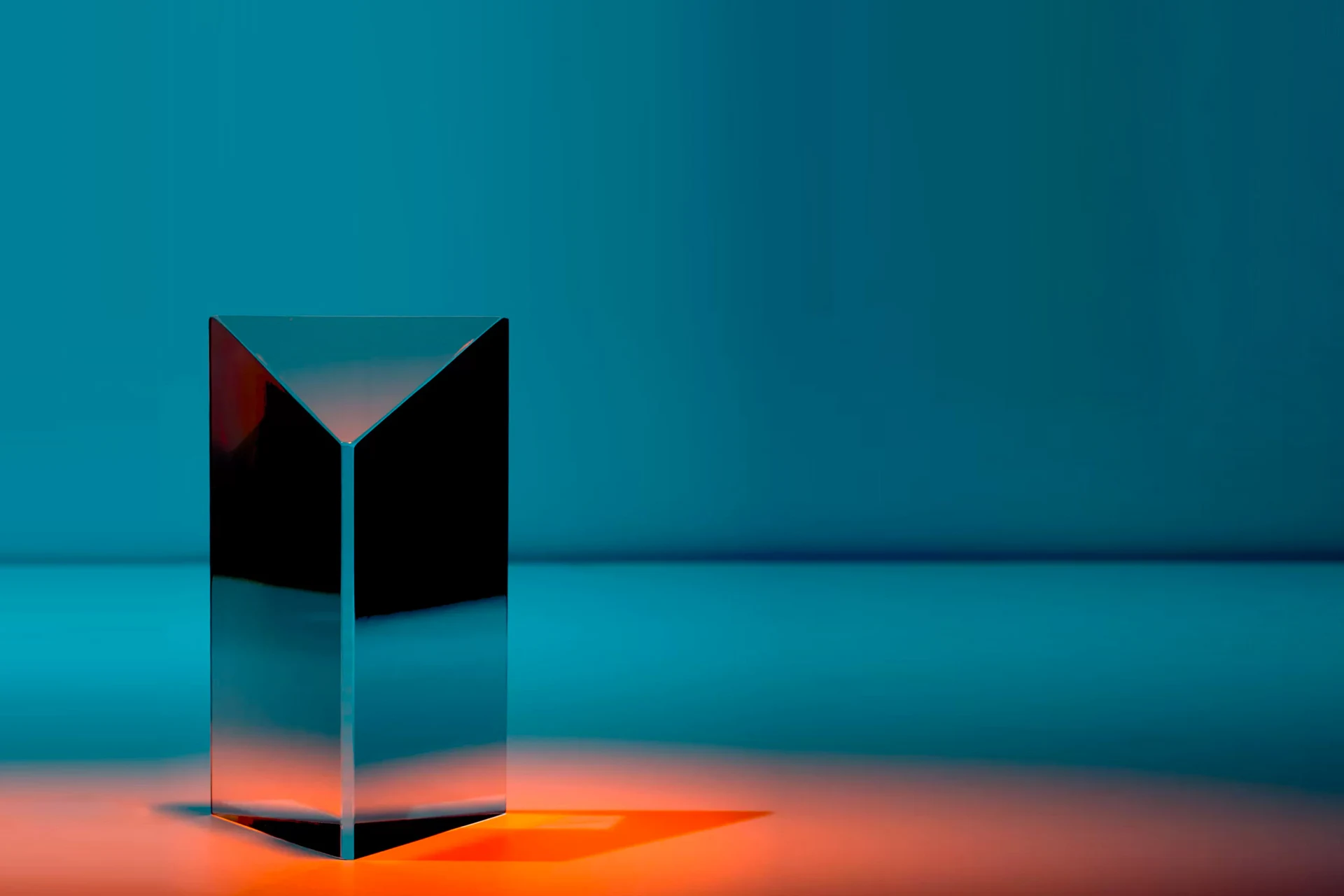 Geometric glass structure illuminated with orange light on a blue backdrop