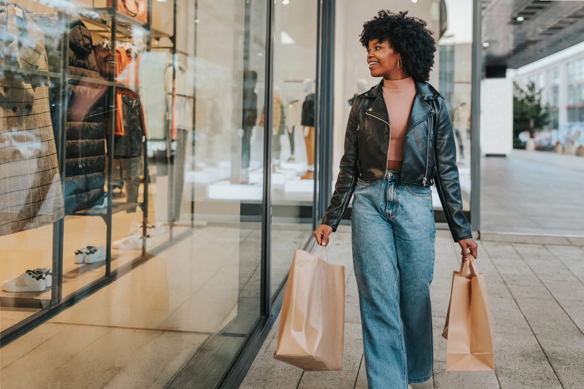 Woman carrying shopping bags outside a retail store displaying clothing
