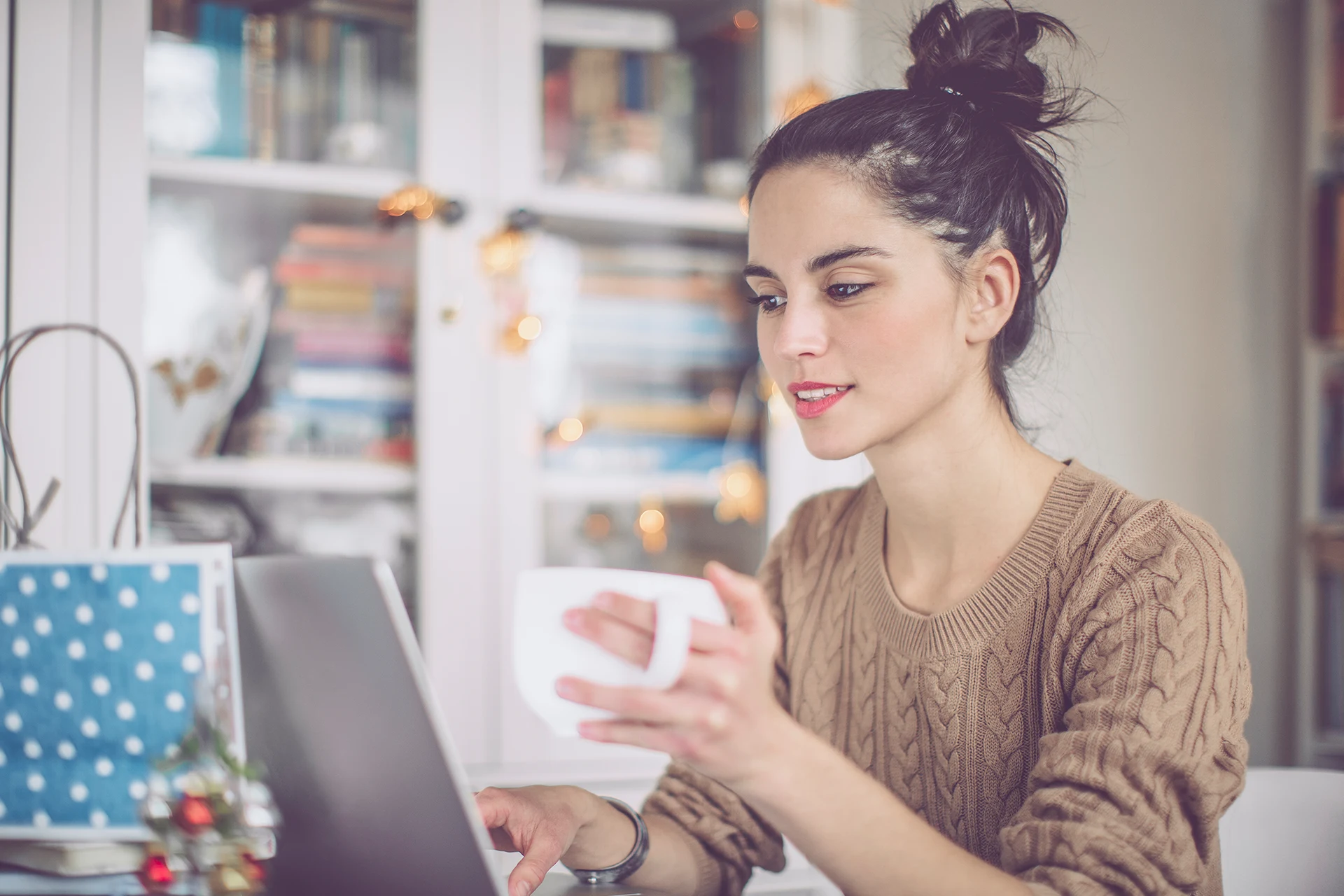 Person holding a coffee cup while working on a laptop at home