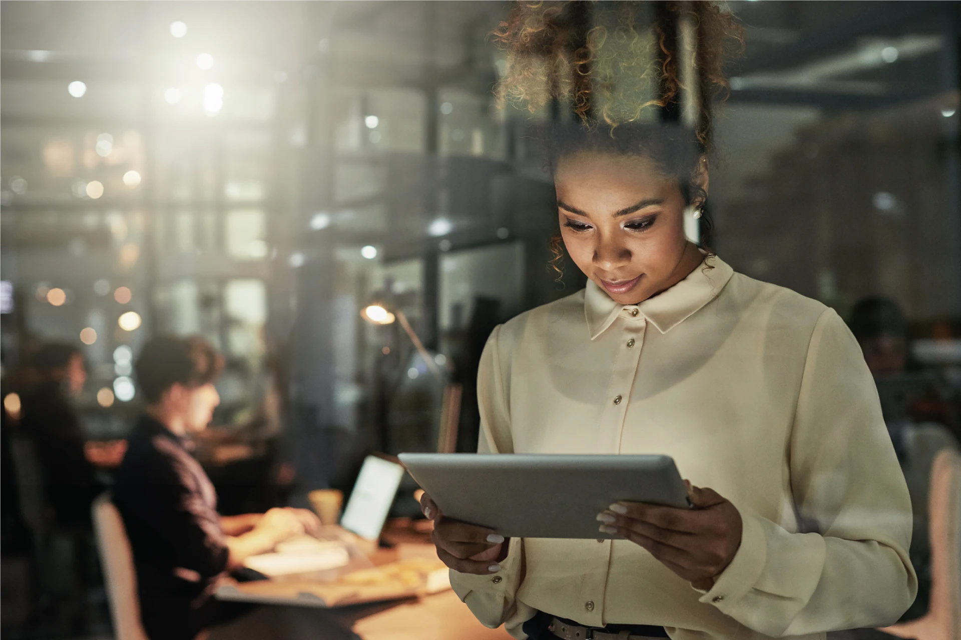 Professional using a tablet in an office setting with a colleague working
