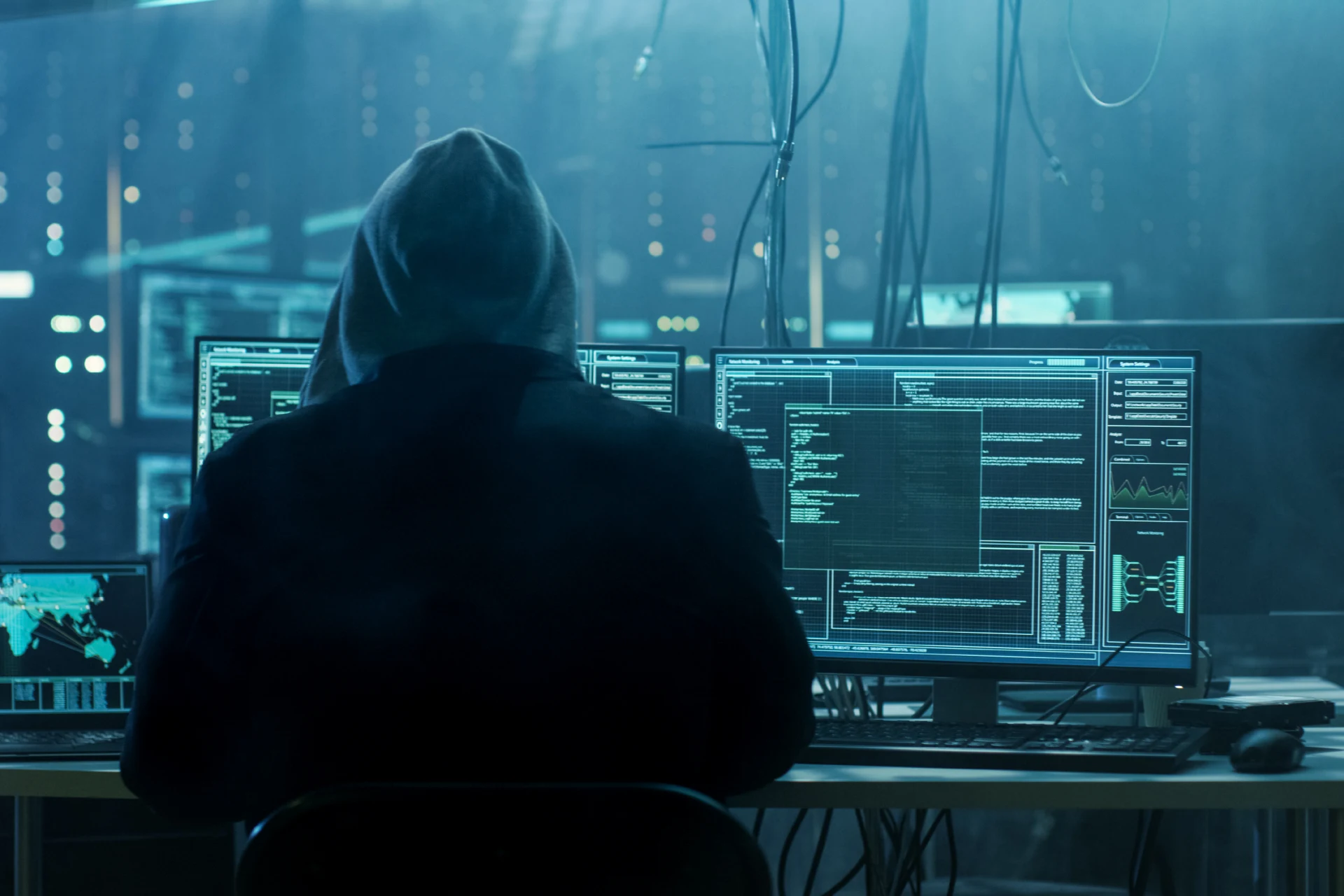 Hacker working at multiple screens in a dimly lit environment.