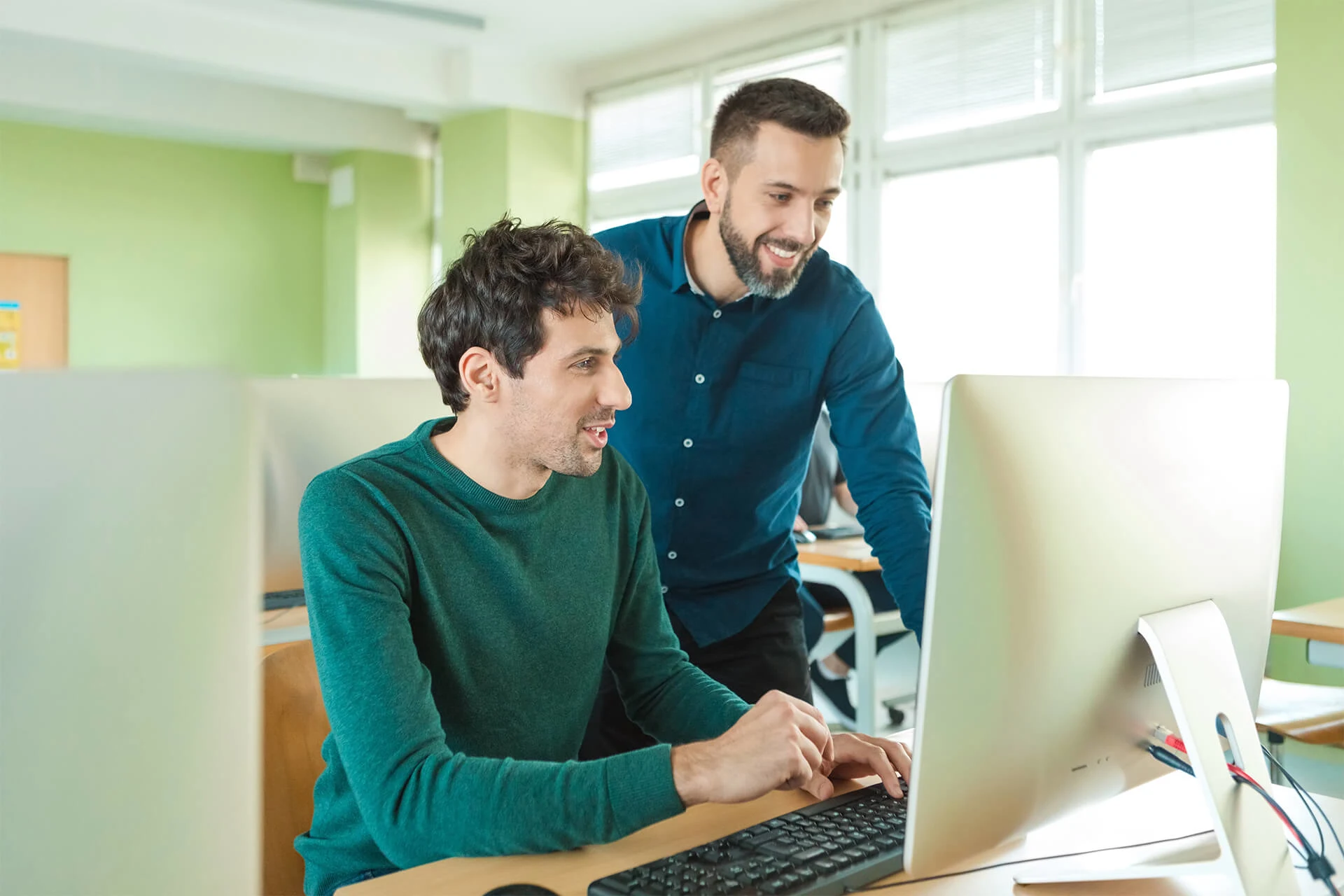 Two individuals collaborating at a computer in a cybersecurity workspace.