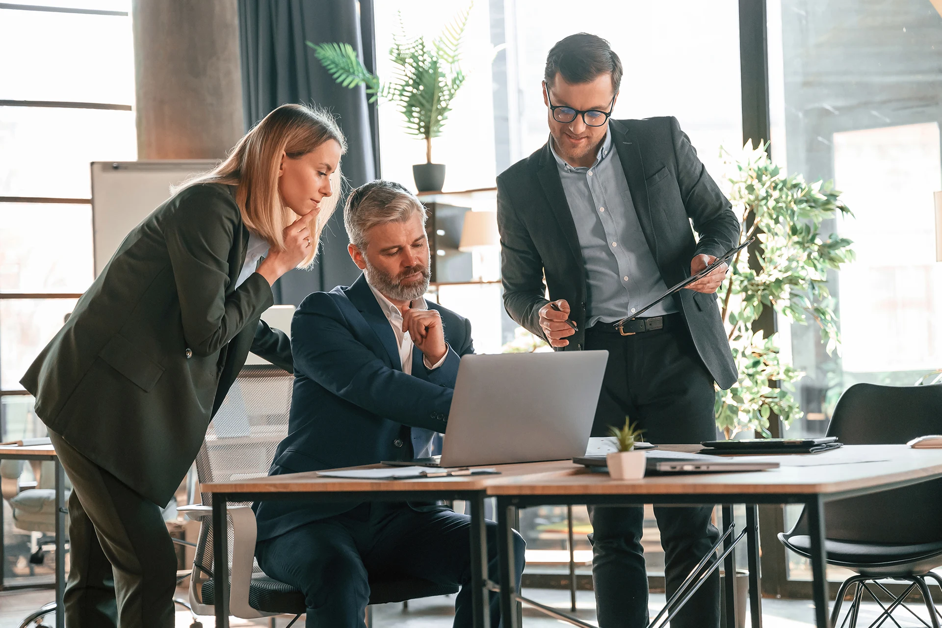 Three professionals discussing AI insights over a laptop in an office