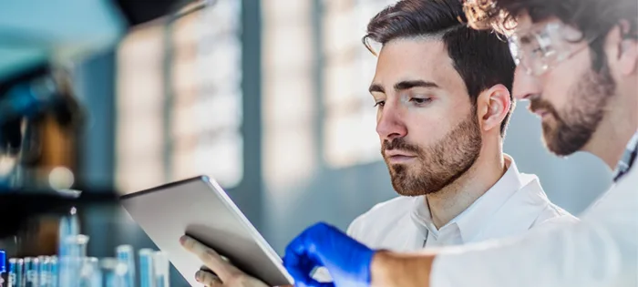 Two lab professionals reviewing data analytics on a tablet inside laboratory