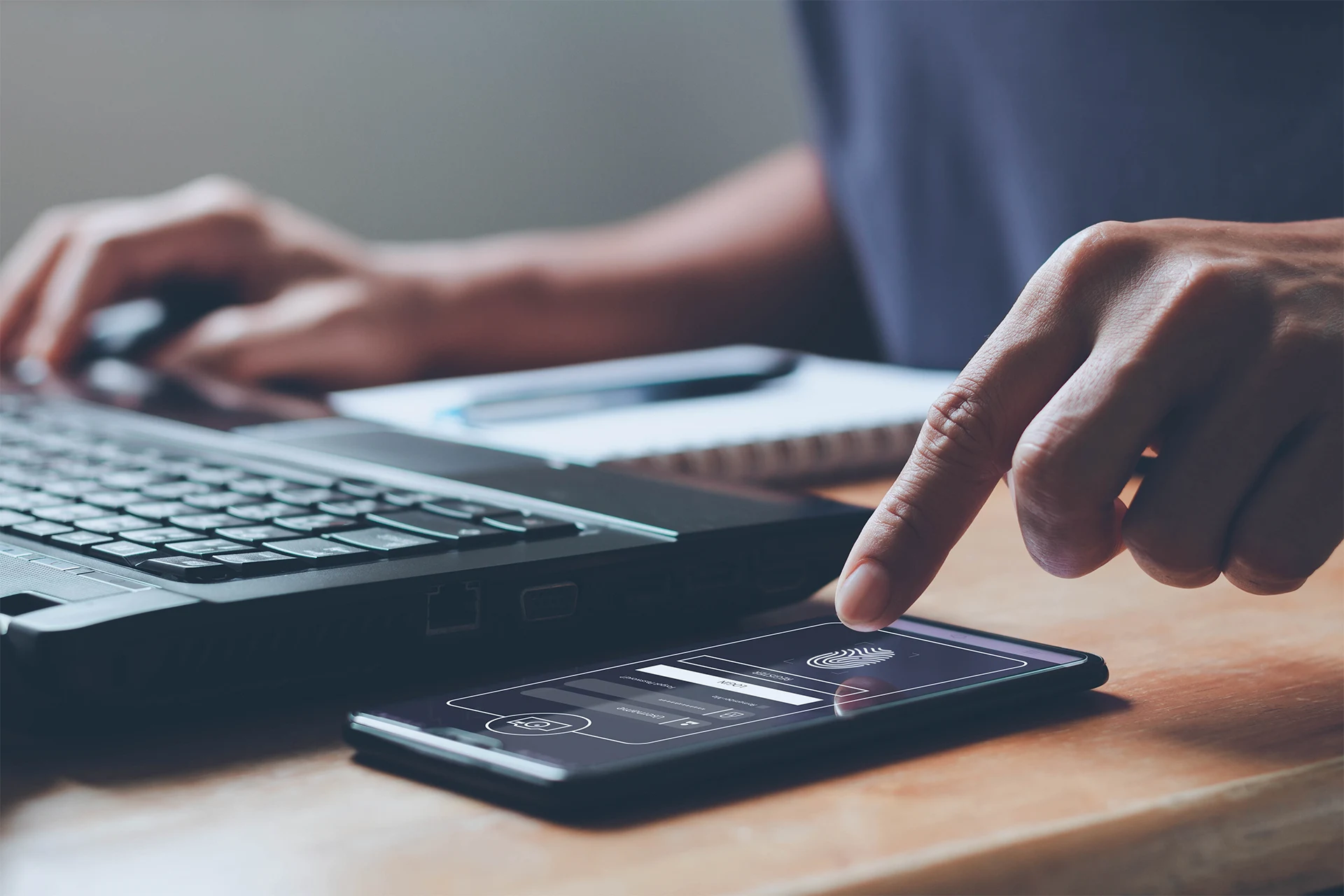 Person using smartphone for authentication while working on laptop
