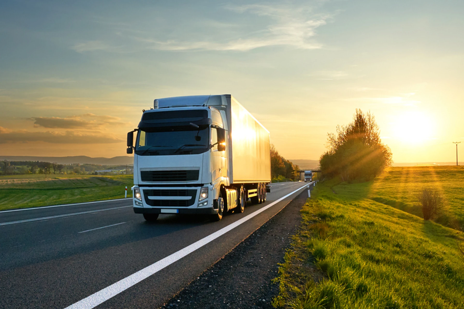 Commercial truck driving on a highway during sunset near green fields.