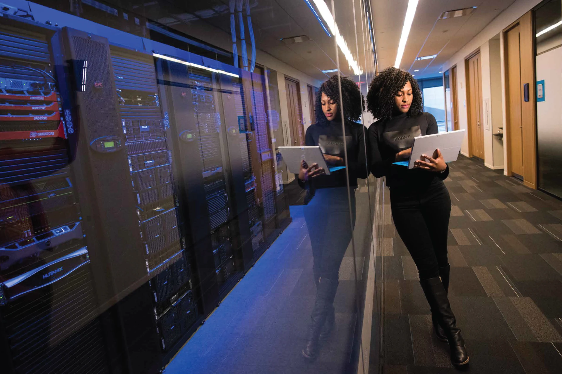 Professional reviewing data on a laptop in a server room setting.