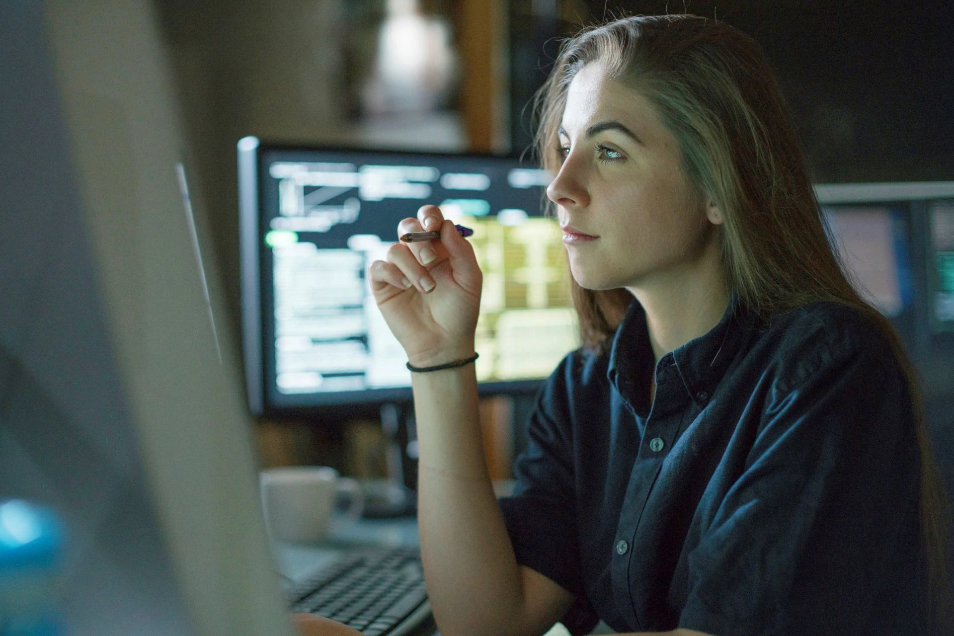 Person analyzing data on computer screens in a workspace environment.