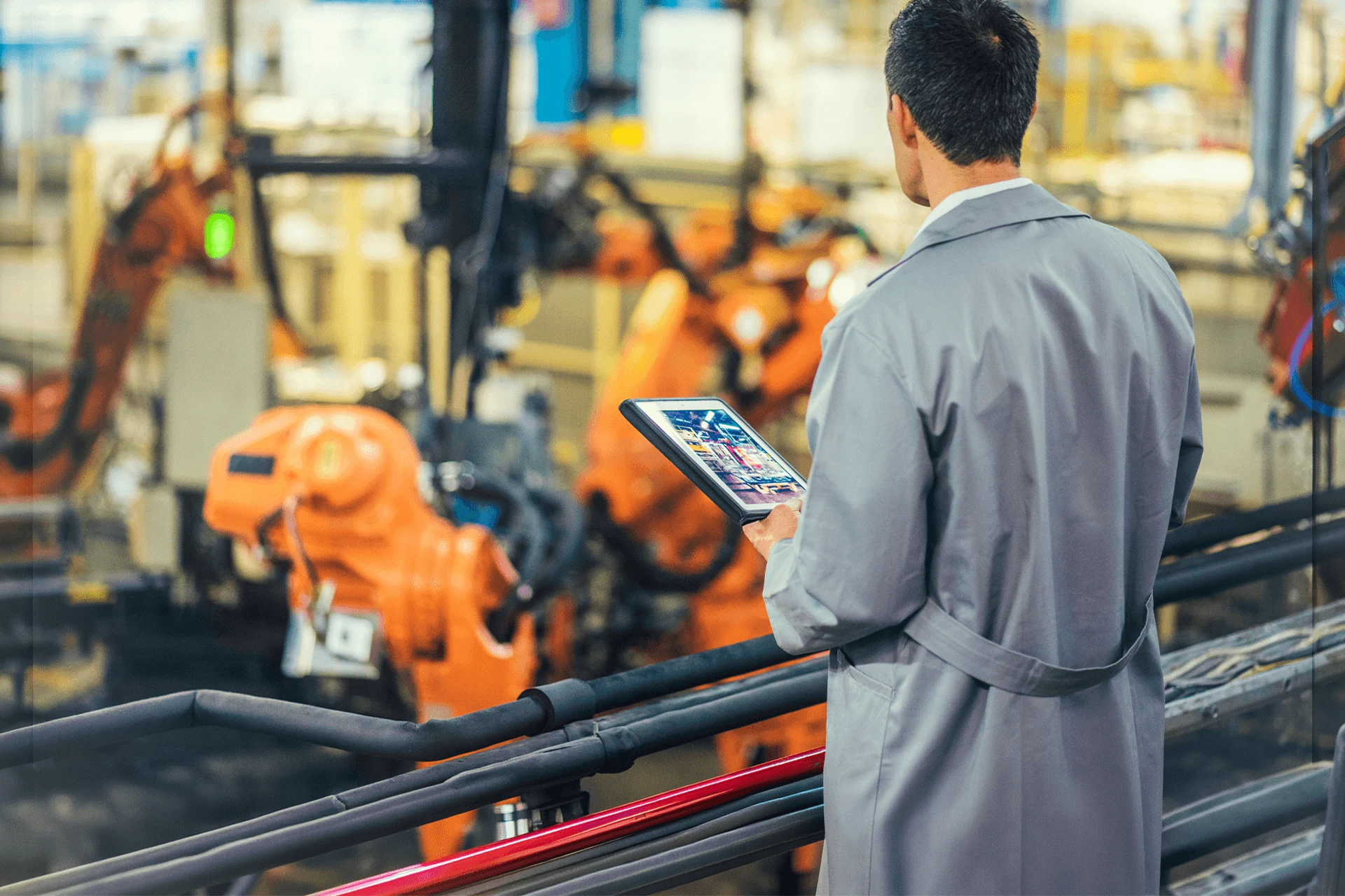 Worker observing robotic arms while using a tablet in a factory setting