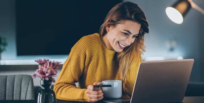 Person in yellow sweater holding mug while working on laptop in cozy space