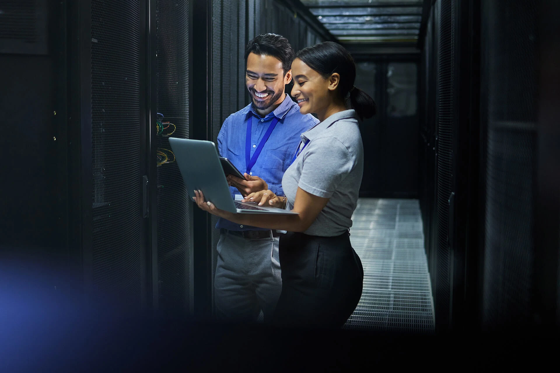 Two professionals collaborating on a laptop in a data center