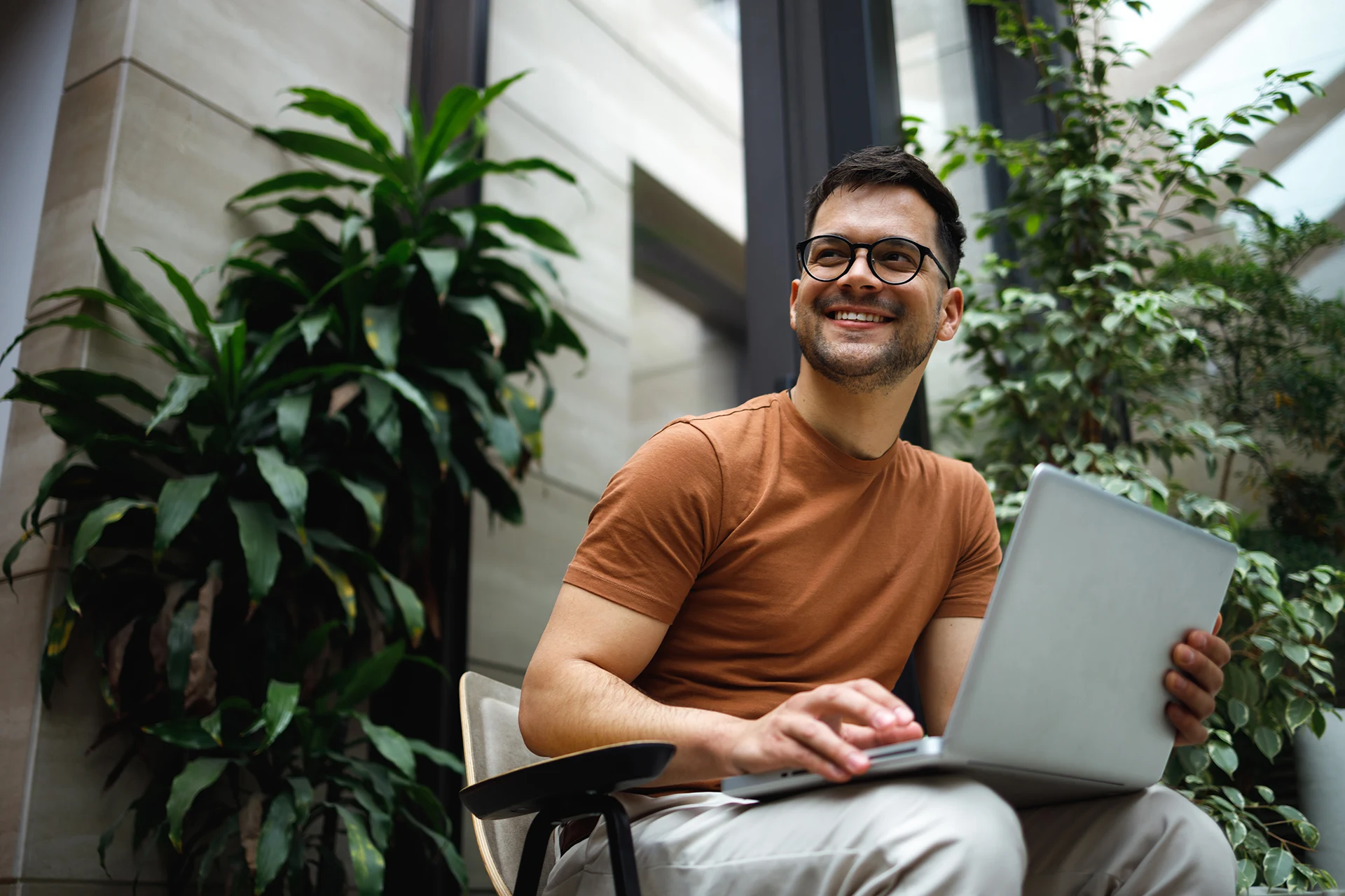 Person using a laptop while seated among indoor plants in an office.