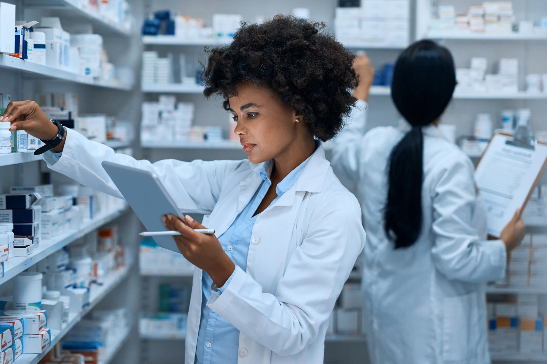 Pharmacist organizing medication on shelves while using a tablet