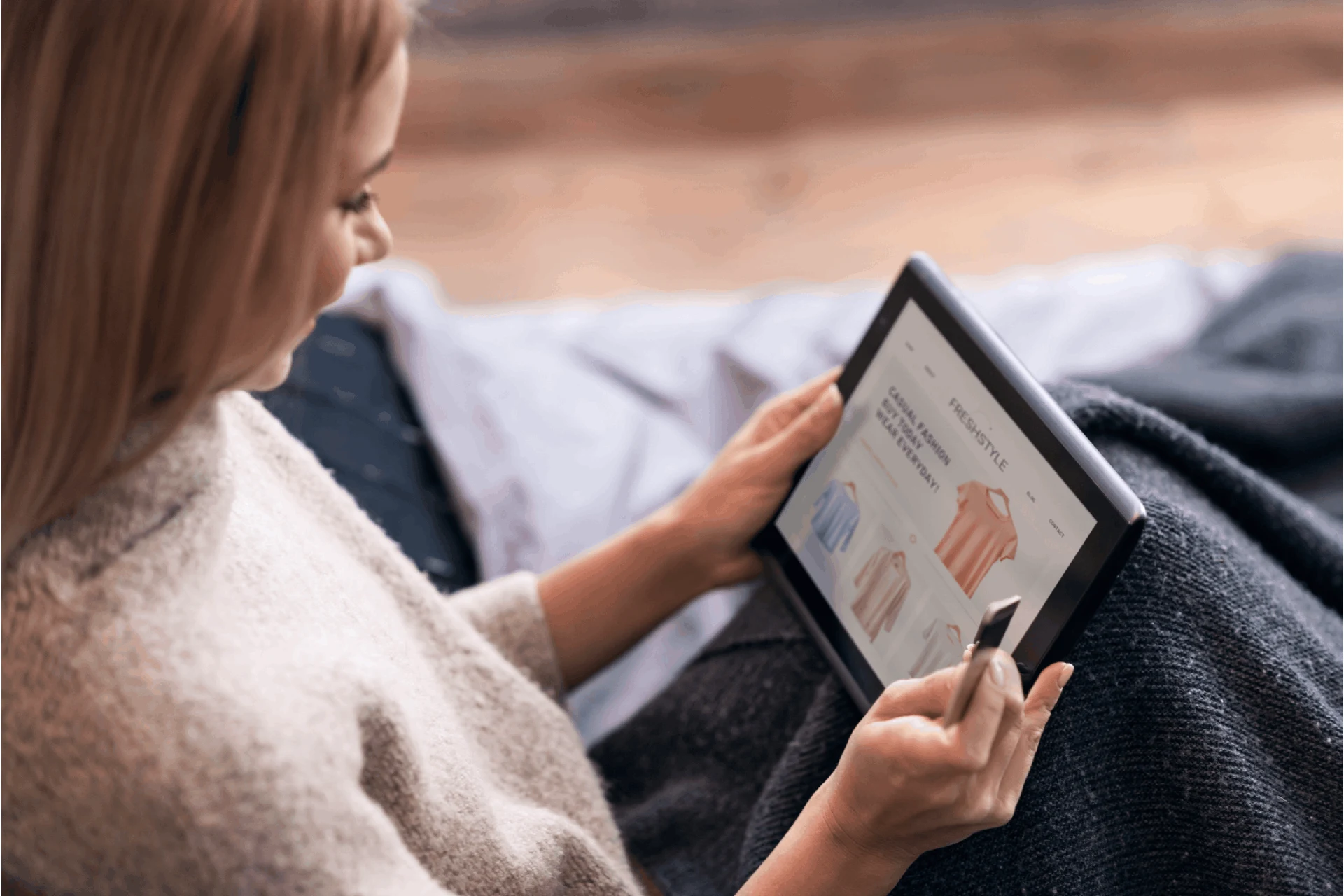 Person browsing clothing options on a tablet while seated on a couch.
