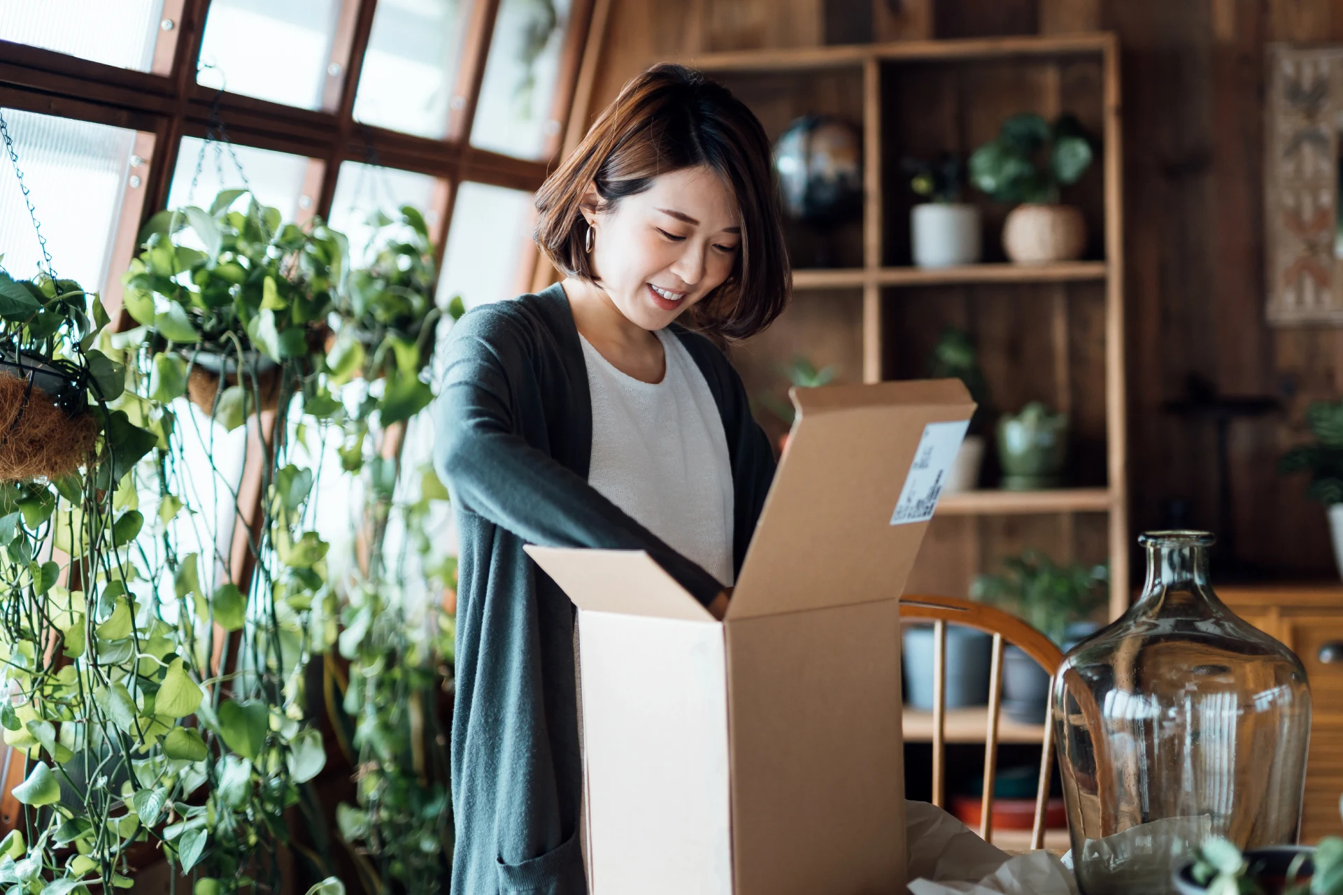 Person unpacking a box in a greenery-filled interior space.