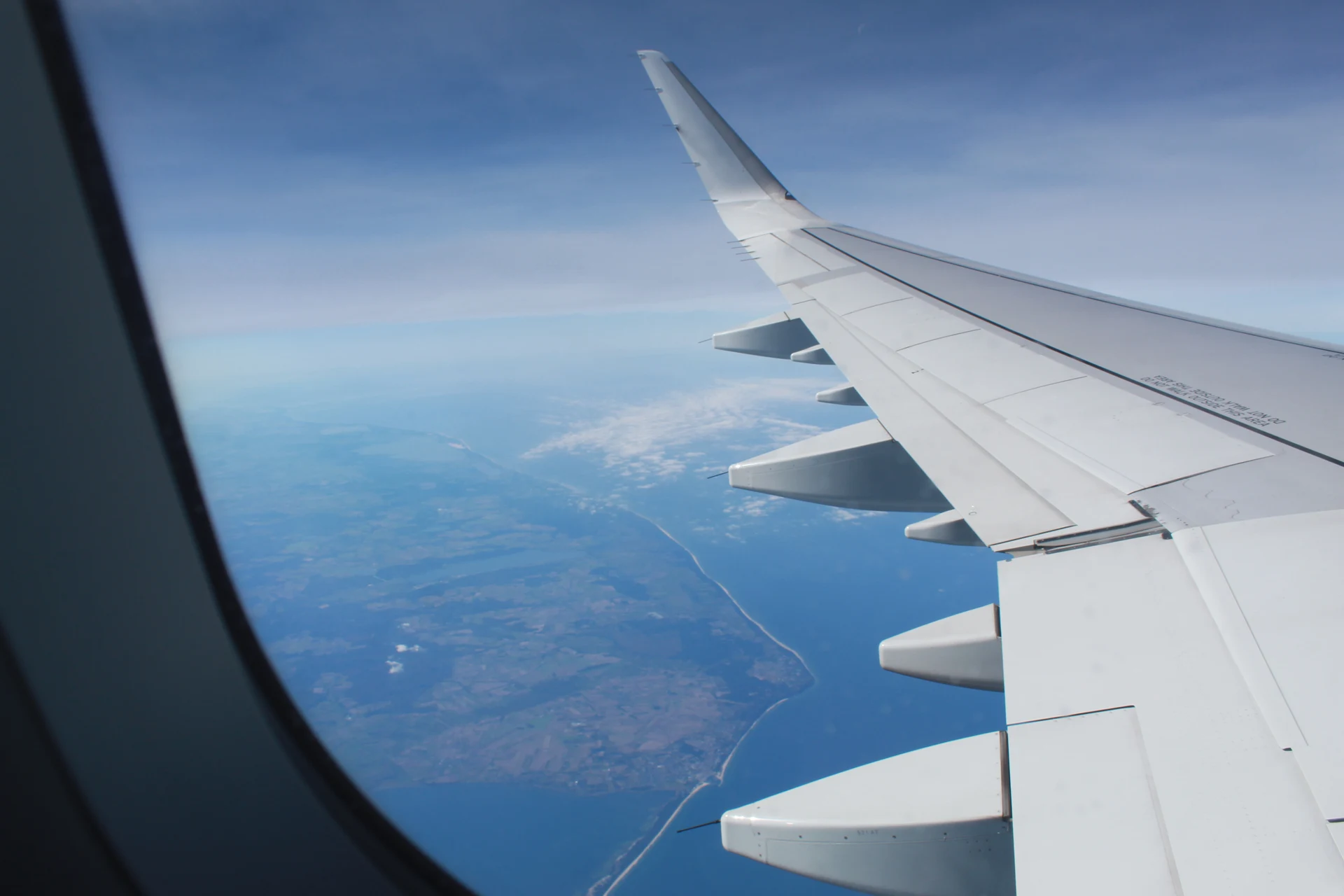 Airplane wing view over land and ocean during flight