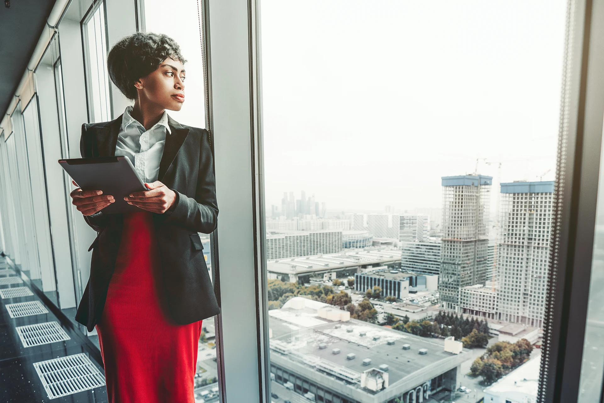 Professional using a tablet while standing near a large window overlooking a