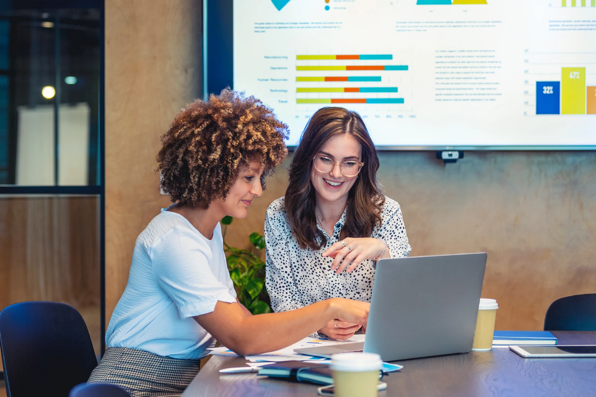 Two professionals discussing data insights with a laptop and charts visible.