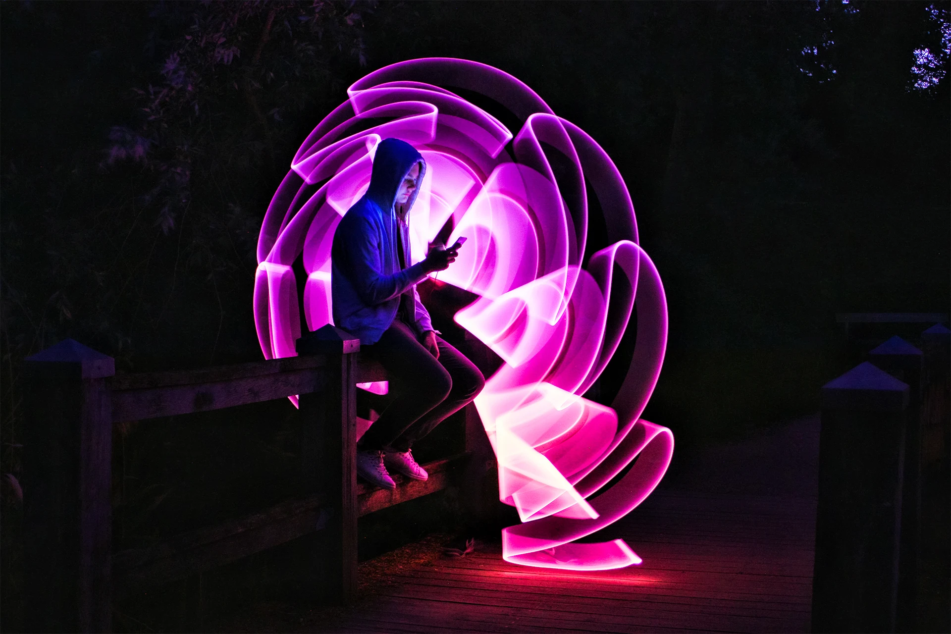 Individual using a smartphone while sitting on a railing at night.