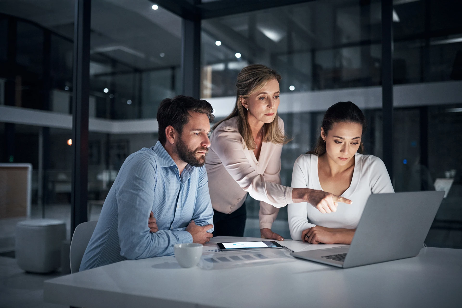 Three professionals engaged in discussion over a laptop in a modern office.