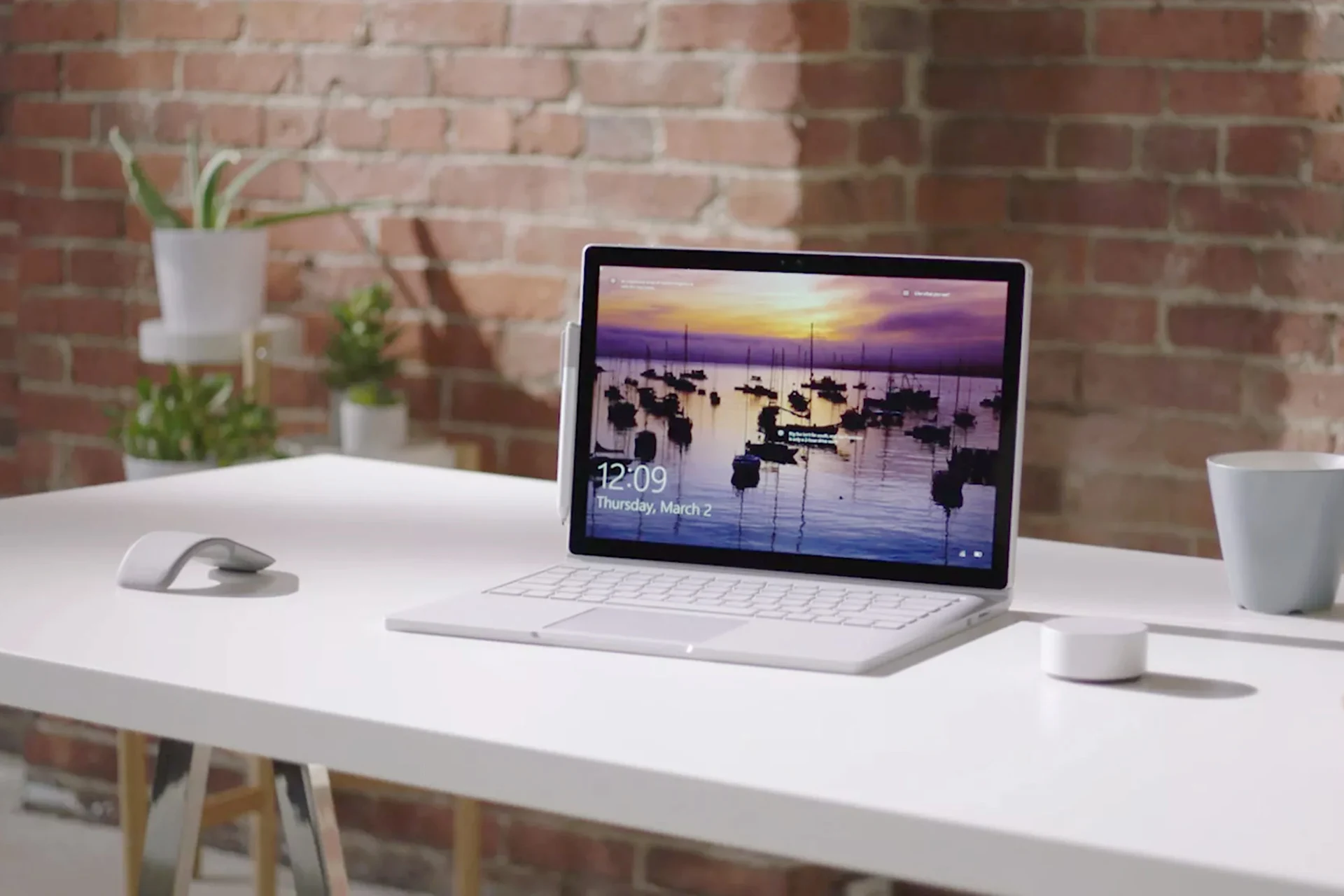 Microsoft Surface laptop on a desk with accessories and a brick wall backdrop
